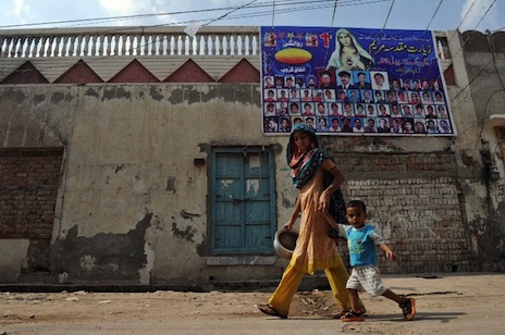 <p>A Christian woman and child walk past a religious poster in Gojra, which has a history of Christian-Muslim clashes (2012 file photo: AFP/Arif Ali) </p>
