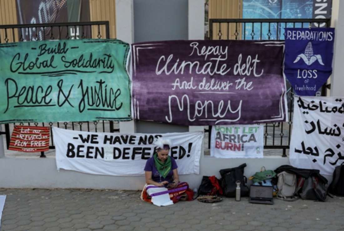 A climate activist sits near banners demanding protection of human rights, climate reparations, and countries' adherence to limit global temperature rise to 1.5 degrees Celsius compared to pre-industrial levels, during the COP27 climate conference in Egypt's Red Sea resort city of Sharm el-Sheikh on Nov 18