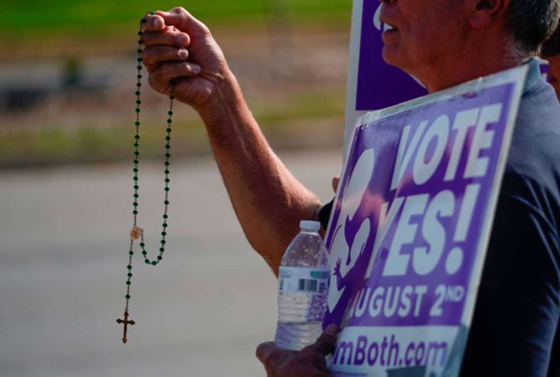 Deacon John Stanley of the Catholic Church prays and waves at cars while holding signs in support of the Vote Yes to a Constitutional Amendment on Abortion on Aug. 1, 2022, in Olathe, Kansas, a day before voters were to vote on whether or not to remove protection for abortion from the state constitution